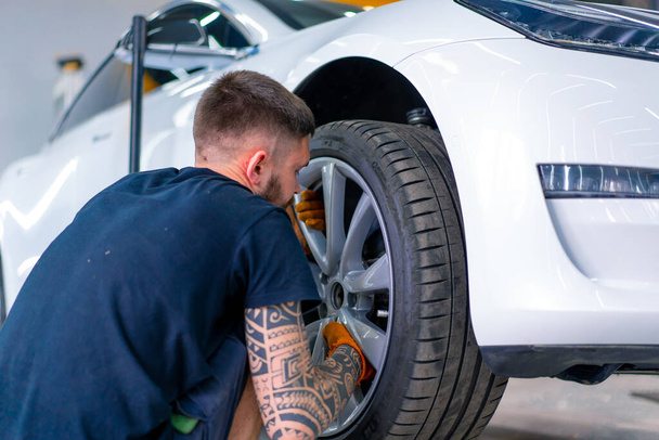 Auto mecânico homem mudando uma roda em um carro branco de luxo usando chave de balão em uma estação de serviço de carro close-up - Foto, Imagem