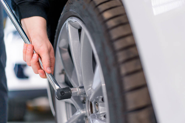 Auto mechanic man changing a wheel on a luxury white car using balloon wrench at a car service station close-up - Photo, image