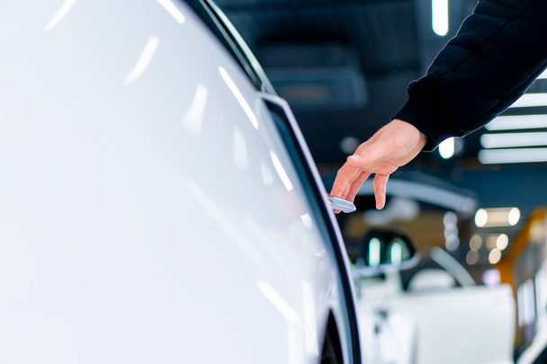 Een man opent de deur van zijn luxe witte auto na detaillering en stomerij bij de autoservice - Foto, afbeelding