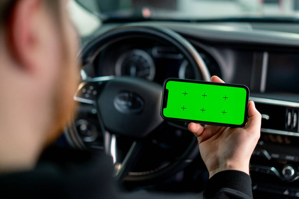 Een man zit in een luxe auto met een groene telefoon in zijn handen - Foto, afbeelding