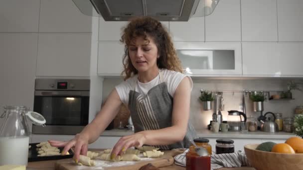 Una felice giovane donna caucasica adulto indossare grembiule in cucina sorriso preparare pasta croissant colazione snack rallentatore - Filmati, video