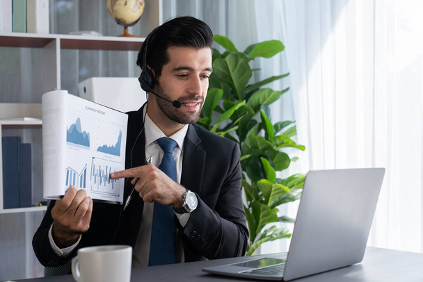 Business man wearing headphone present financial data or BI paper via laptop during online meeting. Remote work concept with virtual meeting presentation of effectiveness remote work. Fervent - Фото, изображение