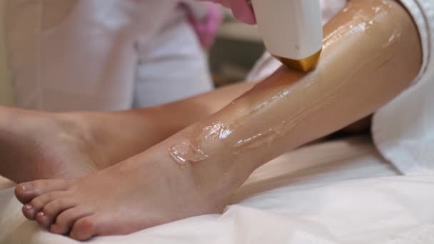 Aesthetic cosmetology. Laser epilation and cosmetology. Hair removal cosmetology procedure. Caucasian woman doing a procedure to remove unwanted hair on her legs using a laser in a beauty salon - Footage, Video