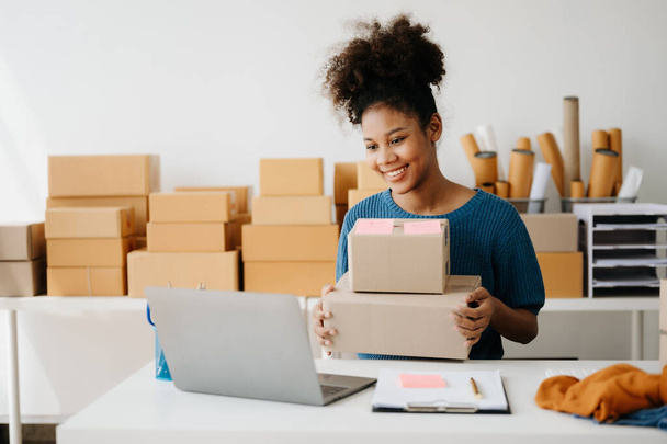 happy smiling African American woman prepare parcel boxes for online delivery while sitting at desk in showrooms  - Foto, Bild