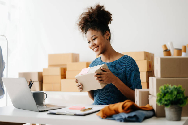 Afrikai amerikai nő előkészíti csomagküldő dobozok online szállítás, miközben ül az asztalnál laptop  - Fotó, kép