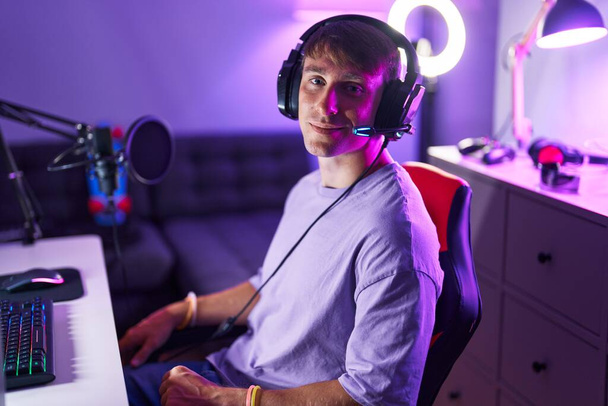 Young caucasian man streamer smiling confident sitting on table at gaming room - 写真・画像