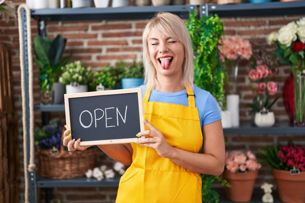 Young caucasian woman working at florist holding open sign sticking tongue out happy with funny expression.  - Photo, Image