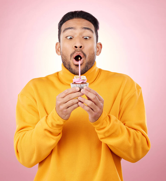 Birthday, cupcake and man blowing candle in studio for celebration, party and dessert. Food, wish and flame with face of male person and cake on pink background for surprise, candy and gift mockup. - Photo, Image