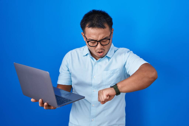 Китайський молодий чоловік, використовуючи комп'ютерний ноутбук, дивлячись на годинник, стурбований, боїться запізнитися  - Фото, зображення