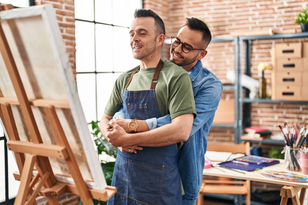 Δύο άντρες καλλιτέχνες αγκαλιάζονται κοιτώντας το στούντιο τέχνης. - Φωτογραφία, εικόνα