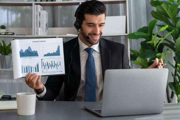Liikemies yllään kuulokkeet esittää taloudellisia tietoja tai BI paperia kannettavan tietokoneen aikana online-kokouksessa. Etätyökonsepti virtuaalisella kokousesityksellä tehokkuuden etätyöstä. Kiihkeä - Valokuva, kuva