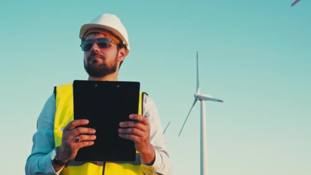 Wind turbines generate green energy with zero carbon footprint. Engineer holding a clipboard and inspecting the windmill park - Felvétel, videó