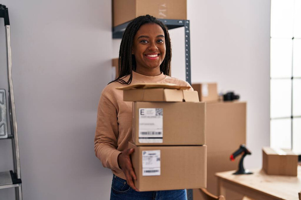 Young african american with braids working at small business ecommerce holding packages smiling with a happy and cool smile on face. showing teeth.  - Foto, Imagem