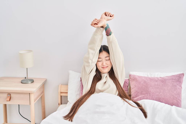 Chinese vrouw wakker stretching armen op slaapkamer - Foto, afbeelding