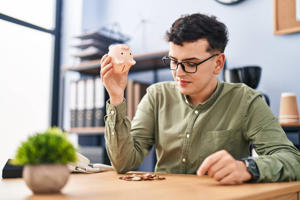 Young non binary man business worker emptying piggy bank at office - Foto, afbeelding