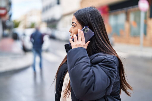 Νεαρή όμορφη ισπανόφωνη γυναίκα μιλάει στο smartphone με χαλαρή έκφραση στο δρόμο - Φωτογραφία, εικόνα