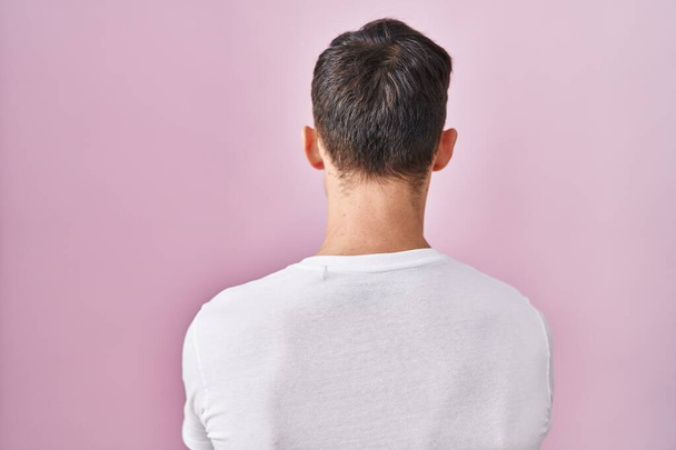 Caucasian man standing over pink background standing backwards looking away with crossed arms  - Photo, Image