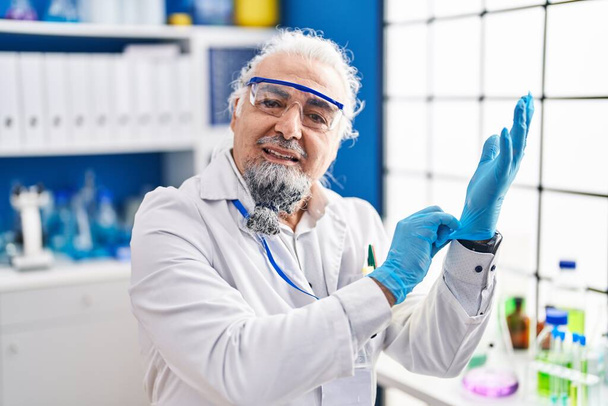 Středního věku šedovlasý muž vědec se usmívá sebevědomě nosit rukavice v laboratoři - Fotografie, Obrázek