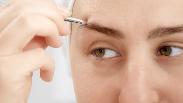 Closeup portrait of smiling young woman forming eyebrows with tweezers after having bath. Concept of beautiful female, makeup at home, skin care and domestic beauty industry - Foto, Bild