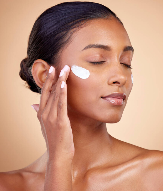Face, cream and woman with eyes closed for skincare cosmetics, dermatology or aesthetic makeup on studio background. Indian female model, lotion and facial sunscreen for clean beauty, glow and shine. - Valokuva, kuva