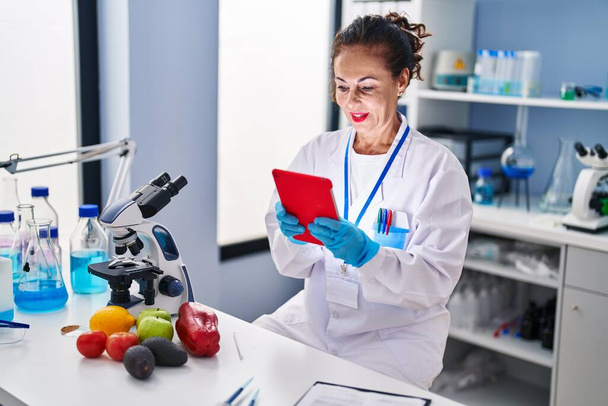 Middle age hispanic woman working with tablet at laboratory - Foto, Imagen