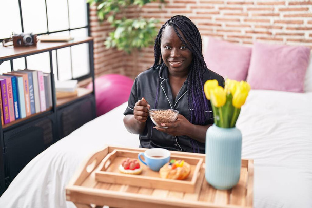 Αφροαμερικανή γυναίκα που παίρνει πρωινό δώρο κάθεται στο κρεβάτι στο υπνοδωμάτιο - Φωτογραφία, εικόνα
