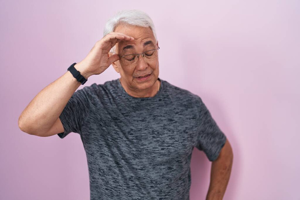 Keski-ikäinen mies, jolla on harmaat hiukset, seisoo vaaleanpunaisen taustan päällä huolissaan ja korosti ongelmaa käsi otsassa, hermostunut ja ahdistunut kriisistä  - Valokuva, kuva