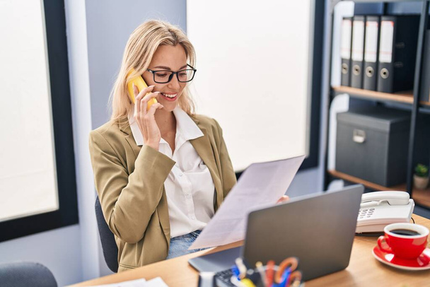 Nuori blondi nainen liiketoiminnan työntekijä puhuu älypuhelin työskentelee toimistossa - Valokuva, kuva