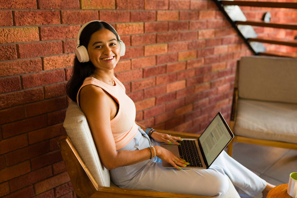Mulher latina feliz com fones de ouvido sorrindo usando seu laptop e a zona wifi em um belo café  - Foto, Imagem