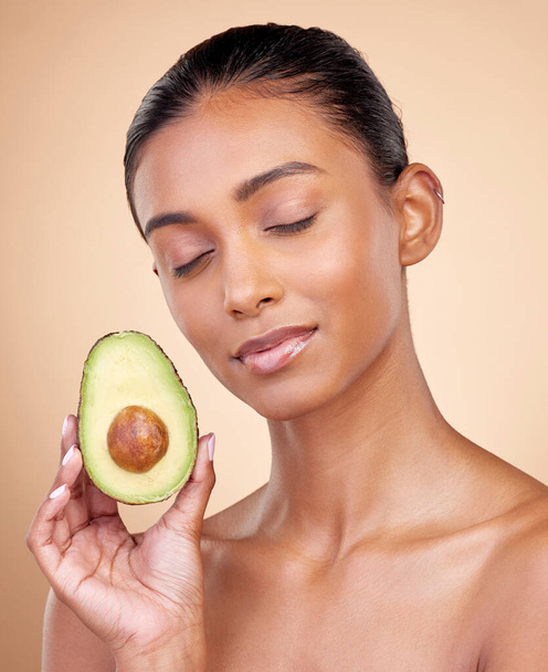 Avocado, facial beauty and woman in studio, background and omega 3 for aesthetic wellness. Face of calm indian female model, natural skincare and fruit for sustainable cosmetics, healthy food or glow. - Photo, Image