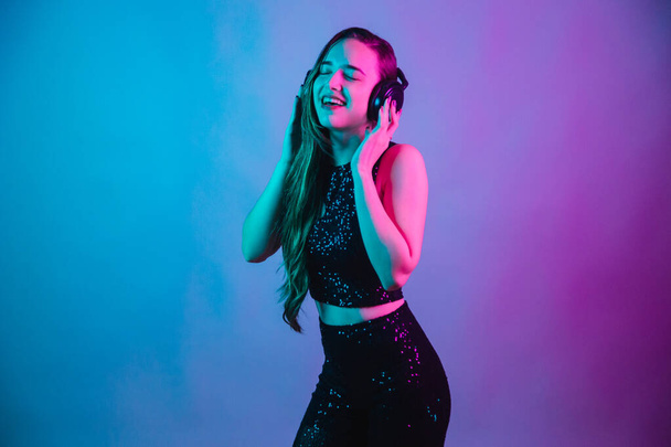Model on blue and pink neon background posing for photo. listening to music with headphones on ear. - Φωτογραφία, εικόνα