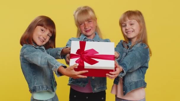 Le ragazze adolescenti che presentano la scatola regalo di compleanno con nastro rosso distende le mani offrono regalo avvolto festa celebrativa, sconto pubblicità vacanze vendita. Sorelle bambine. Tre fratelli e sorelle bambini - Filmati, video