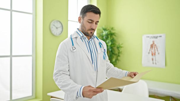 Young hispanic man doctor reading medical report at clinic - Foto, imagen