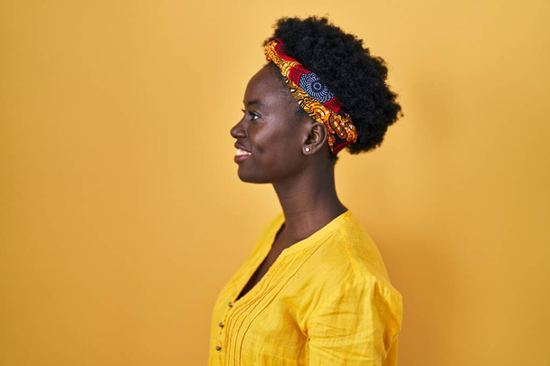 Afrikanische junge Frau mit afrikanischem Turban, die zur Seite schaut, entspannte Profilpose mit natürlichem Gesicht und selbstbewusstem Lächeln.  - Foto, Bild