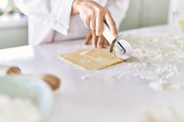 Młoda kobieta nosi mundur kucharz cięcia ciasta makaronowego w kuchni - Zdjęcie, obraz