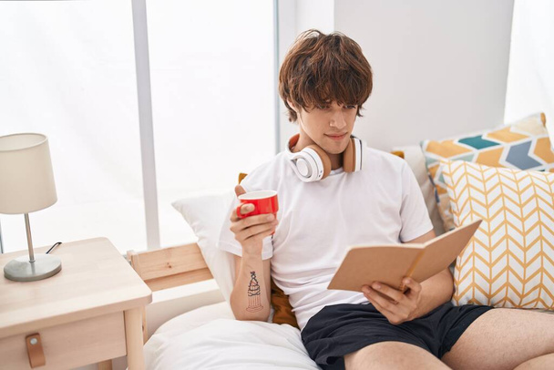 Young blond man reading book drinking coffee at bedroom - Φωτογραφία, εικόνα