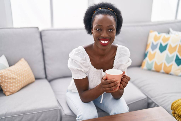 African american woman drinking coffee sitting on sofa at home - Fotoğraf, Görsel