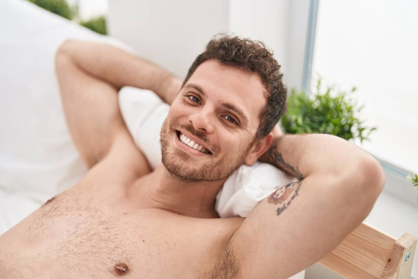 Joven hombre hispano relajado con las manos en la cabeza acostado en la cama en el dormitorio - Foto, imagen