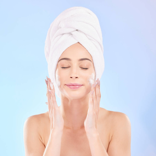 Face, skincare and woman with soap, towel and isolated in studio on a blue background. Eyes closed, cosmetic and model washing, cleaning or hygiene with facial foam for health, dermatology or beauty. - Foto, Imagen