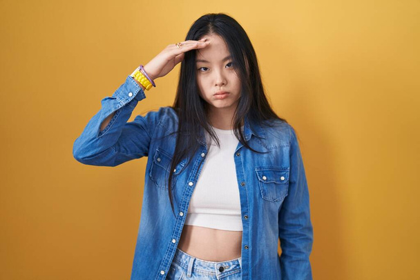Молодая азиатка, стоящая на жёлтом фоне, беспокоилась о проблеме с рукой на лбу, нервничала и беспокоилась о кризисе.  - Фото, изображение