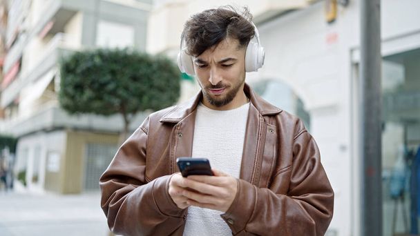 Young arab man listening to music with relaxed expression at street - Foto, afbeelding