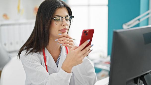 Jeune femme caucasienne médecin faire appel vidéo avec smartphone souriant à la clinique - Photo, image