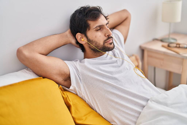 Young hispanic man listening to music relaxed on bed at bedroom - Foto, Bild
