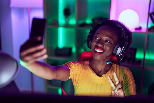 Afrikkalainen amerikkalainen nainen serpentiini hymyilee luottavainen tehdä selfie älypuhelimella pelihuoneessa - Valokuva, kuva