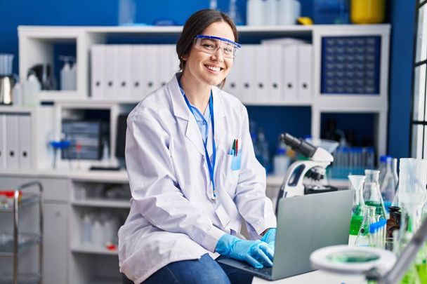 Nuori nainen tiedemies käyttää kannettavaa tietokonetta laboratoriossa - Valokuva, kuva