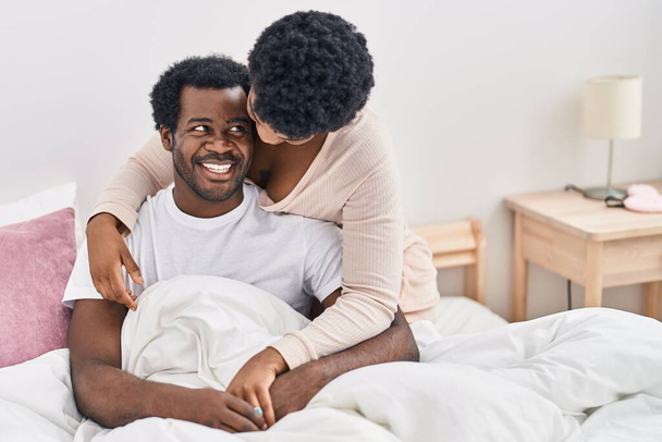 Африканские американец мужчина и женщина обнимают друг друга сидя на кровати в спальне - Фото, изображение