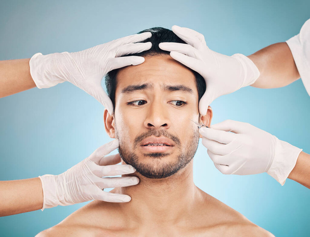 Face, hands and plastic surgery with a worried man in studio on a blue background for beauty enhancement. Aesthetic, botox or change with a young male patient looking nervous in a clinic for skincare. - Foto, afbeelding