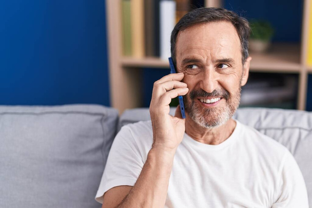 Uomo di mezza età che parla su smartphone seduto sul divano di casa - Foto, immagini