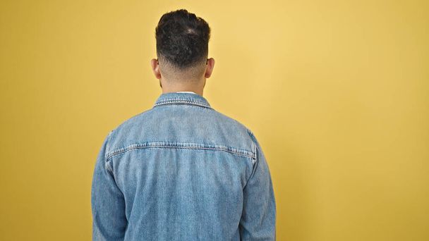 Hombre latino joven de pie hacia atrás sobre fondo amarillo aislado - Foto, Imagen