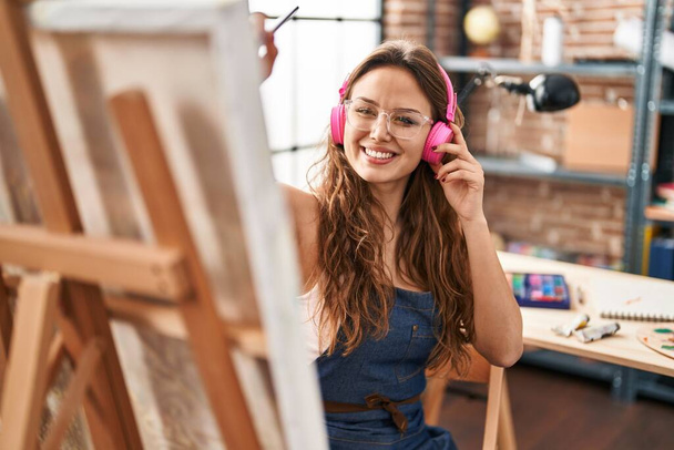 Young beautiful hispanic woman artist listening to music drawing at art studio - Fotó, kép